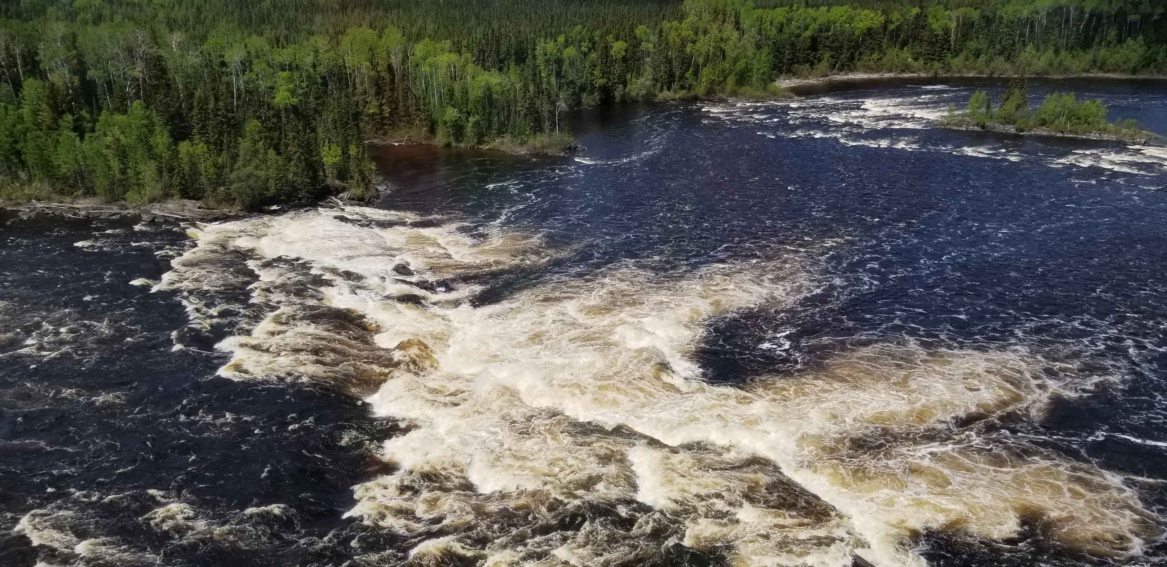 Birds-eye view of moving waters in a lake and forest of trees in Marten Falls.