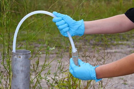 Photo of person’s hands wearing gloves taking sample of groundwater through a plastic tube.