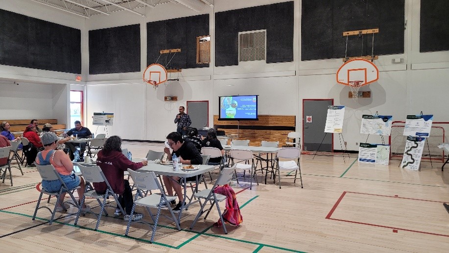 1. Photo of people talking in a gymnasium with tables and posters in Marten Falls First Nation.