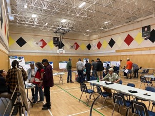 2. Photo of people talking in a gymnasium with tables and posters in Aroland First Nation.
