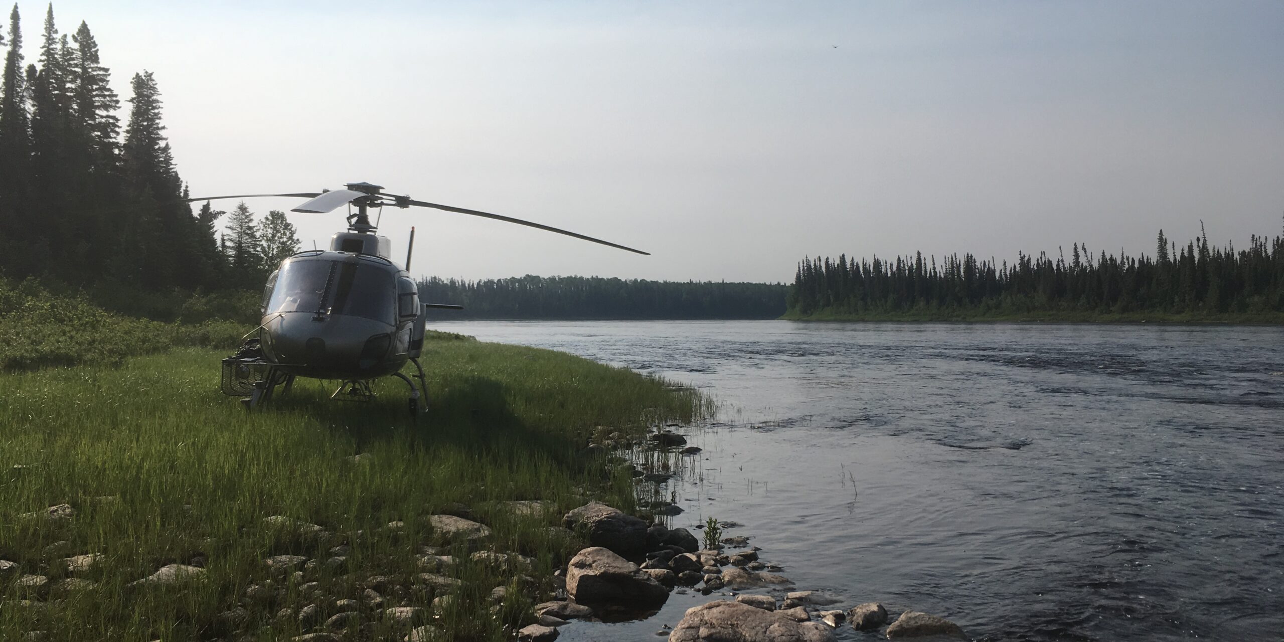 A photo of a helicopter landed on the grass beside a river.