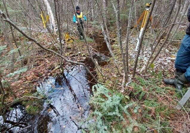 MFFN - Geotechnical investigation Photo of two men in the forest by stream with survey equipment.